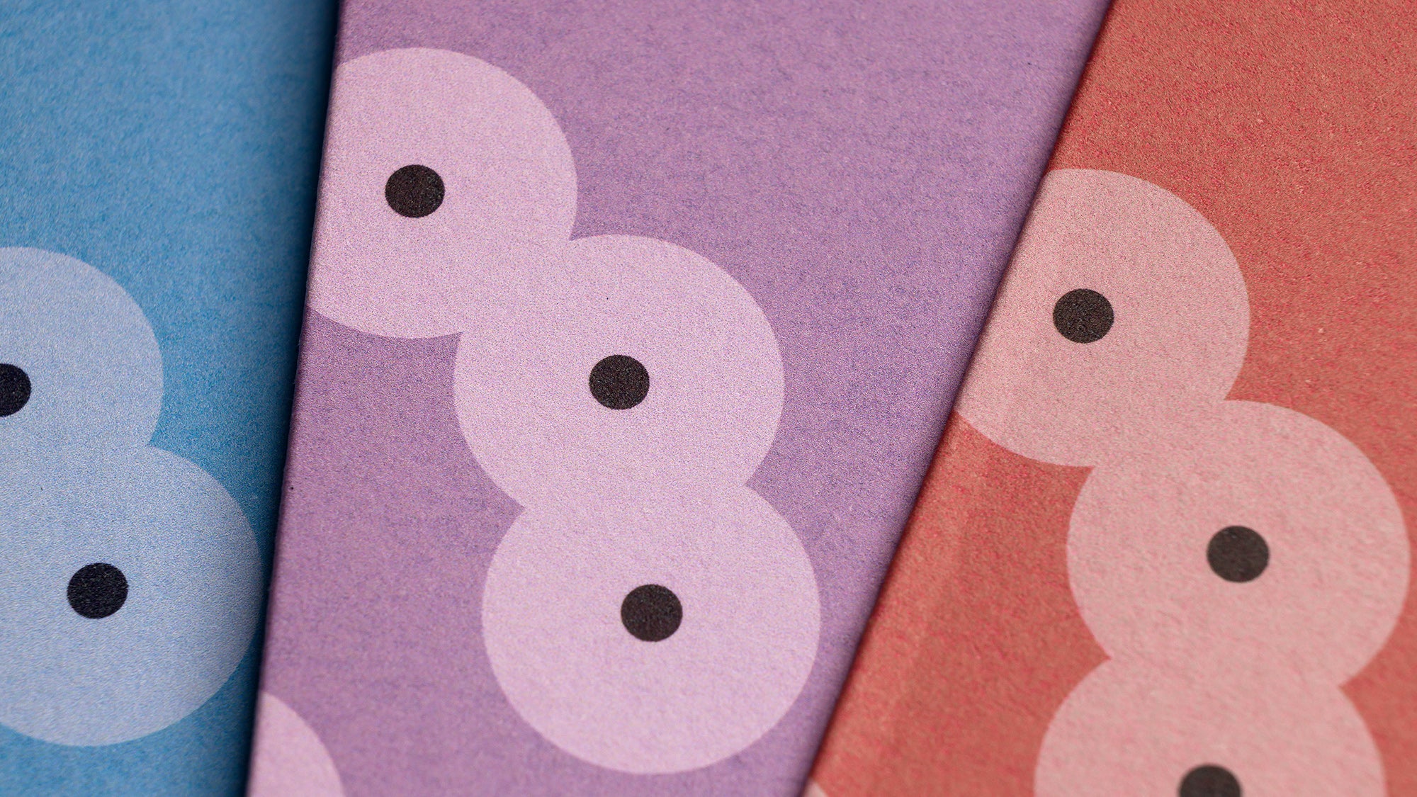 Detail of three overlapping Spawn greeting cards, showing the pattern of clustering circles, in three colours: blue, lilac and orange