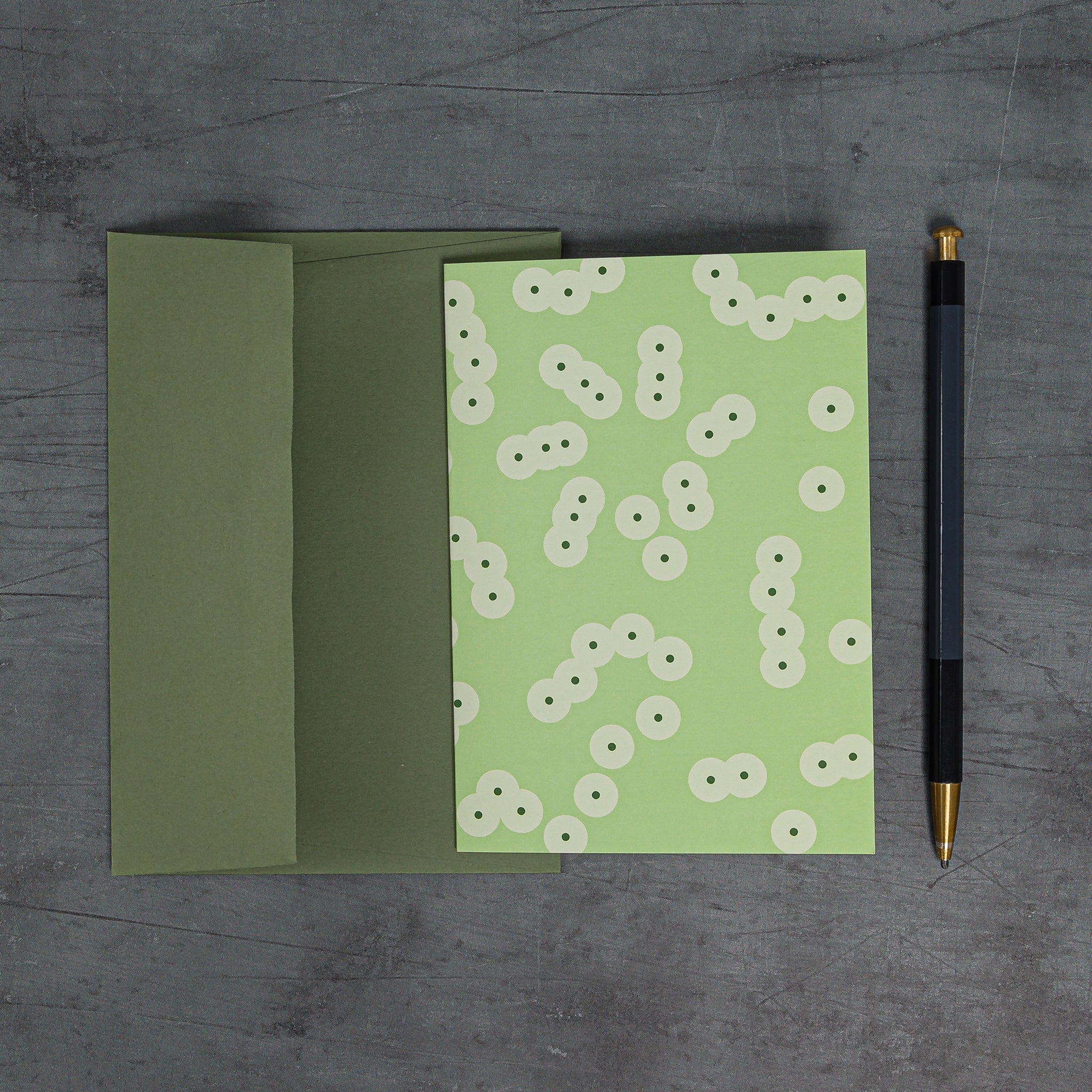 Aerial view of Spawn (green) greeting card with coordinating sage green envelope. Design: geometric pattern of clustering circles, inspired by frog spawn