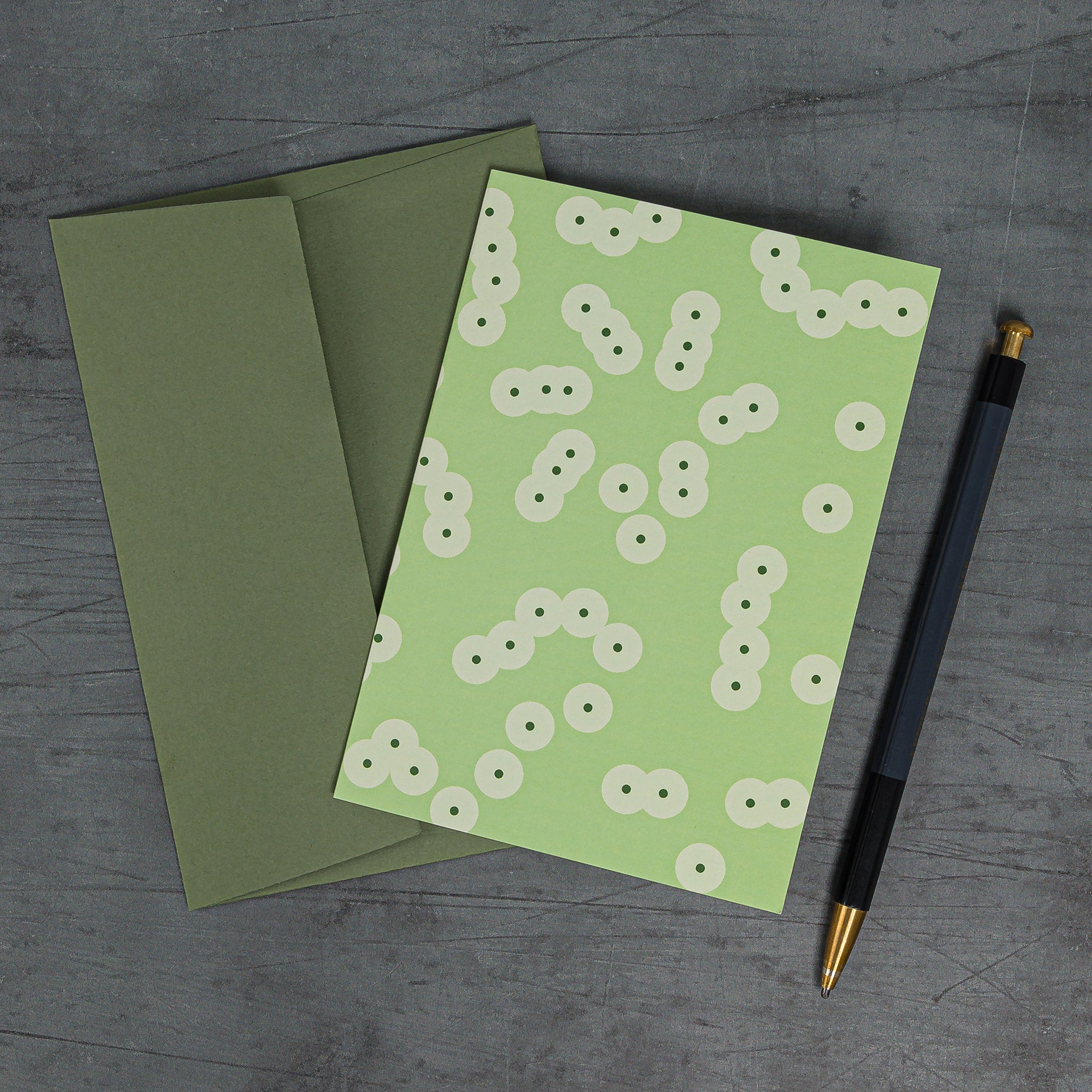 Spawn (green) greeting card, slanted, with matching green envelope. Pattern: clusters of circles suggestive of frog spawn