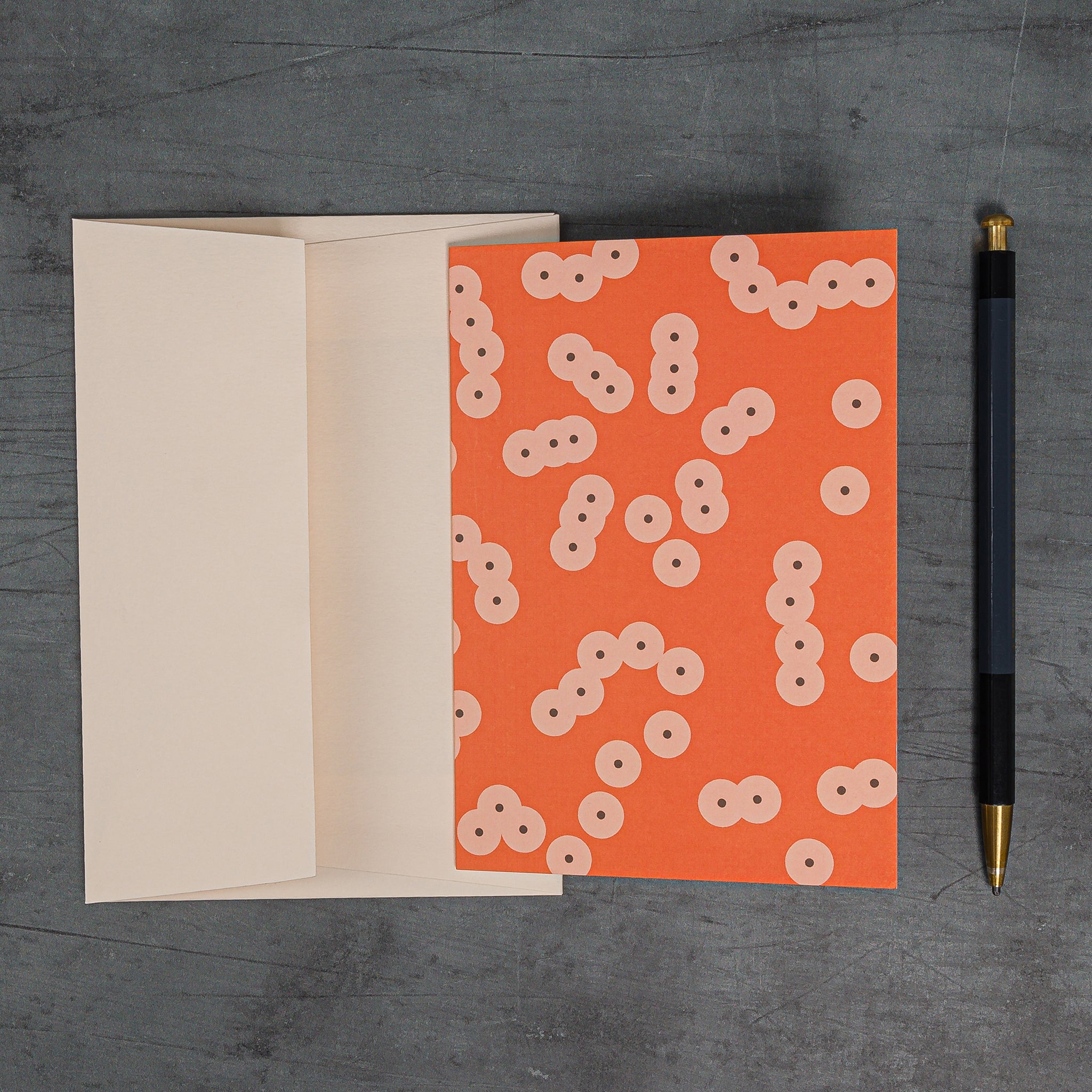 Aerial view of Stack (orange) greeting card and matching peach-coloured Colorplan envelope by G F Smith. Pattern: clusters of circles suggestive of frog spawn