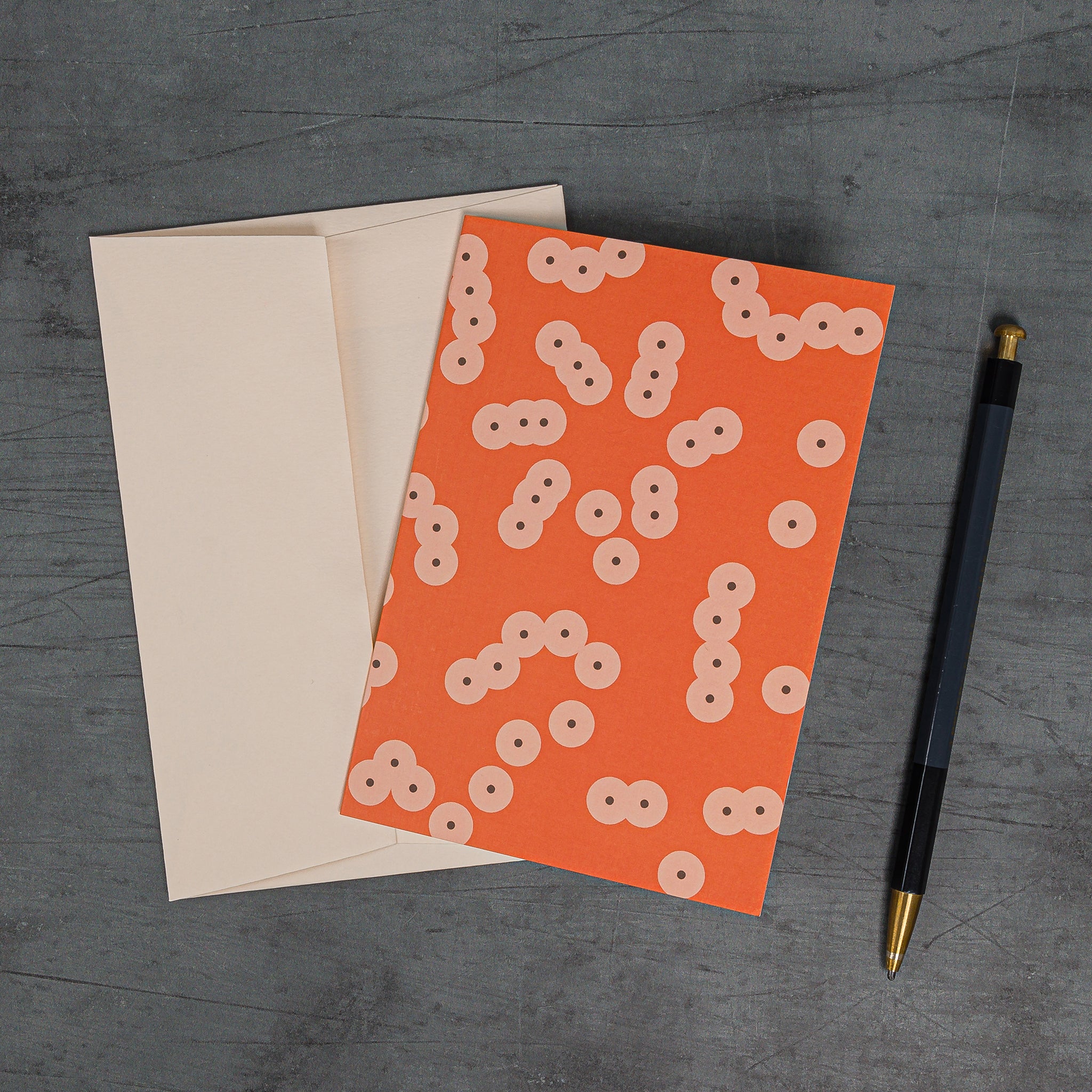 Aerial view, slanted, of Spawn (orange) greeting card and matching peach-toned envelope. Irregular pattern of clustering circles