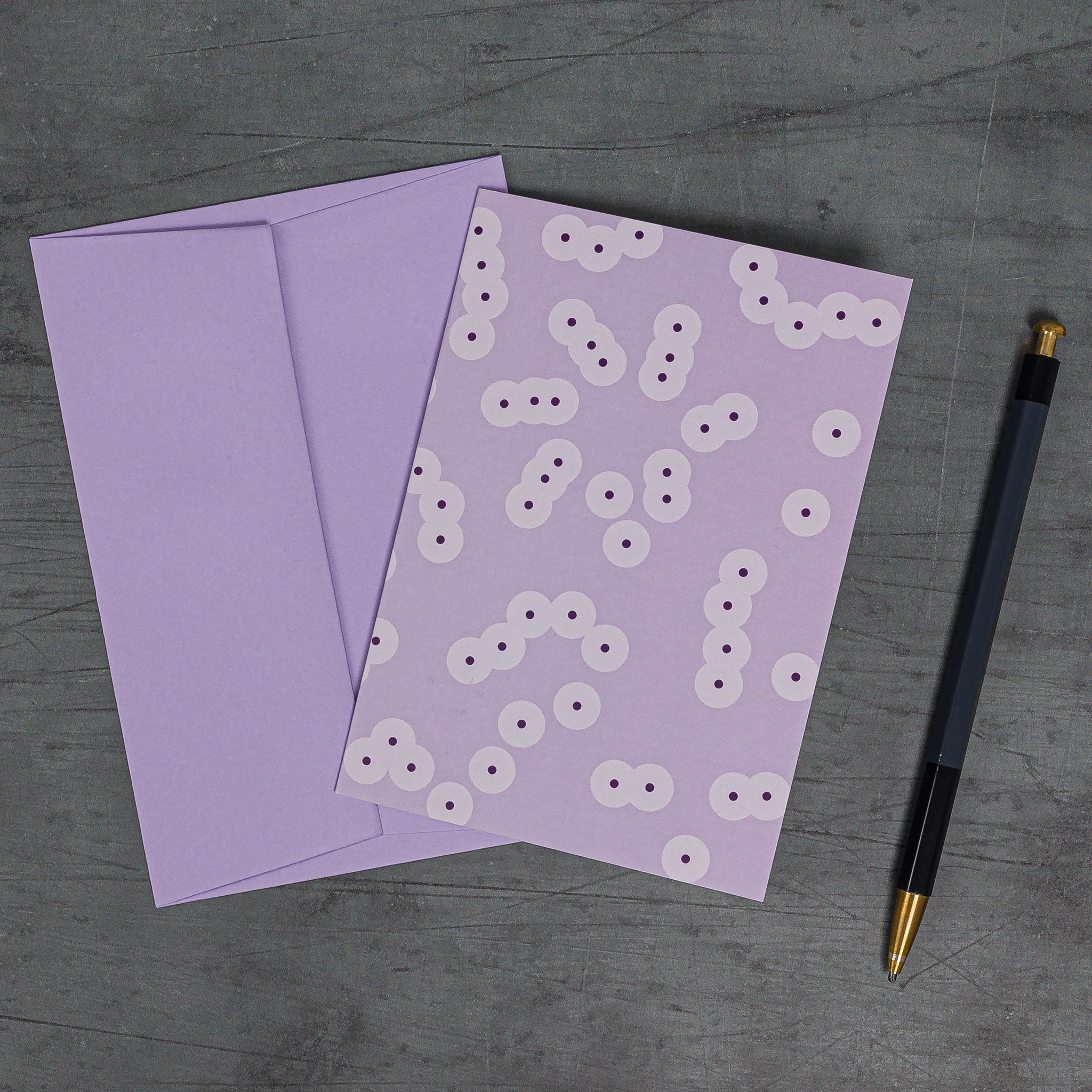 Aerial view, slanted, of Spawn (lilac) greeting card and matching envelope. Pattern: clusters of circle motifs, resembling frog spawn