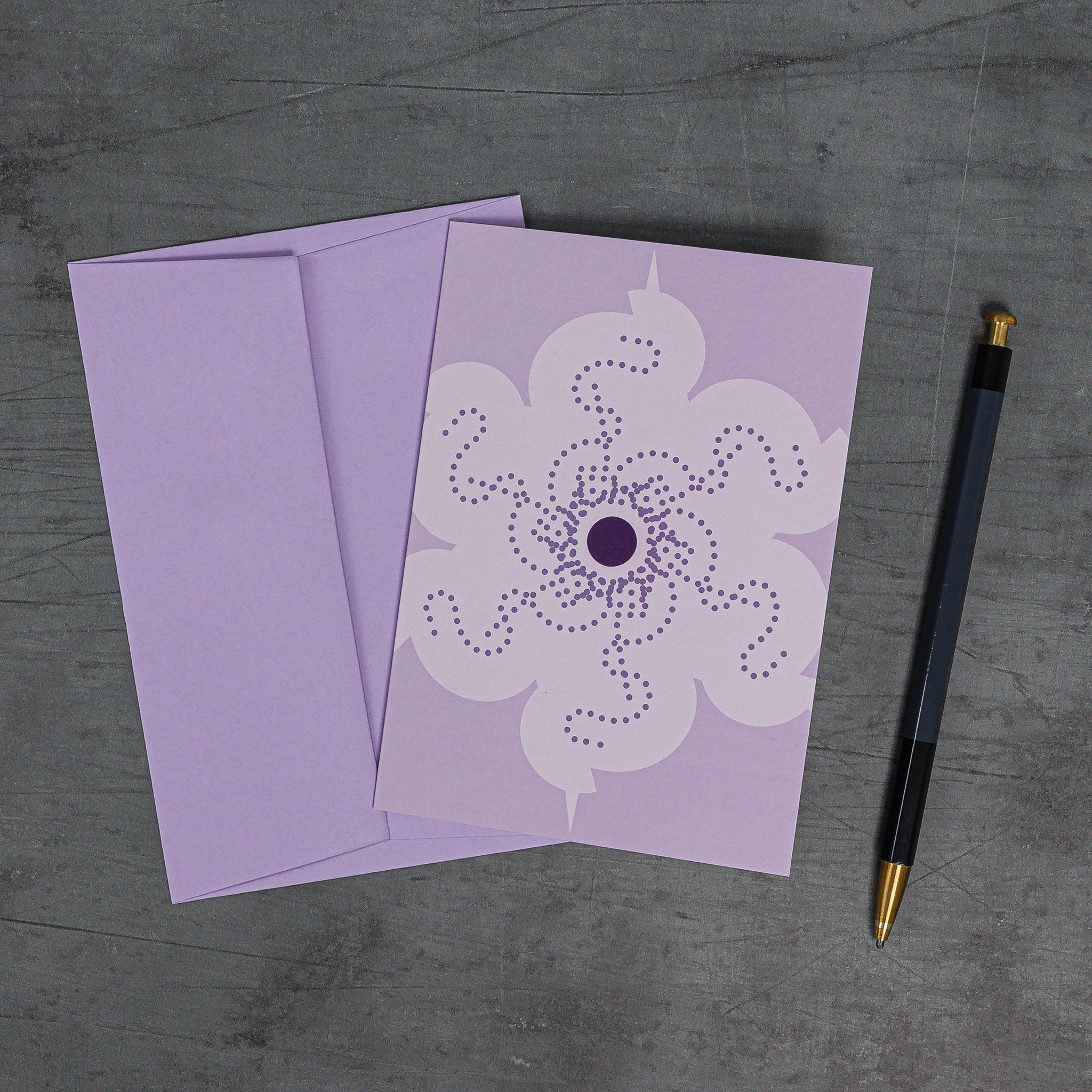Orbit 2 greeting card, slanting view, with matching lilac envelope. Geometric floral motifs rotating around a central disc