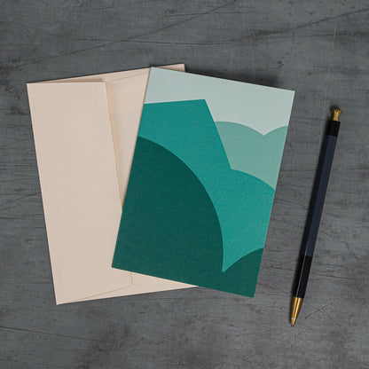 Aerial view, slanted, of the Stack (teal) greeting card. Layerd curves and angles resembling a schematised landscape. Teal colour scheme and coordinating peach-coloured envelope