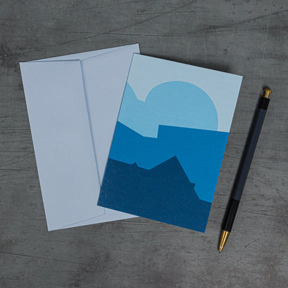 Aerial view, slanted, of Stack (blue) greeting card and coordinating pale blue envelope. Simple geometric design of stacked curves and slanting angles