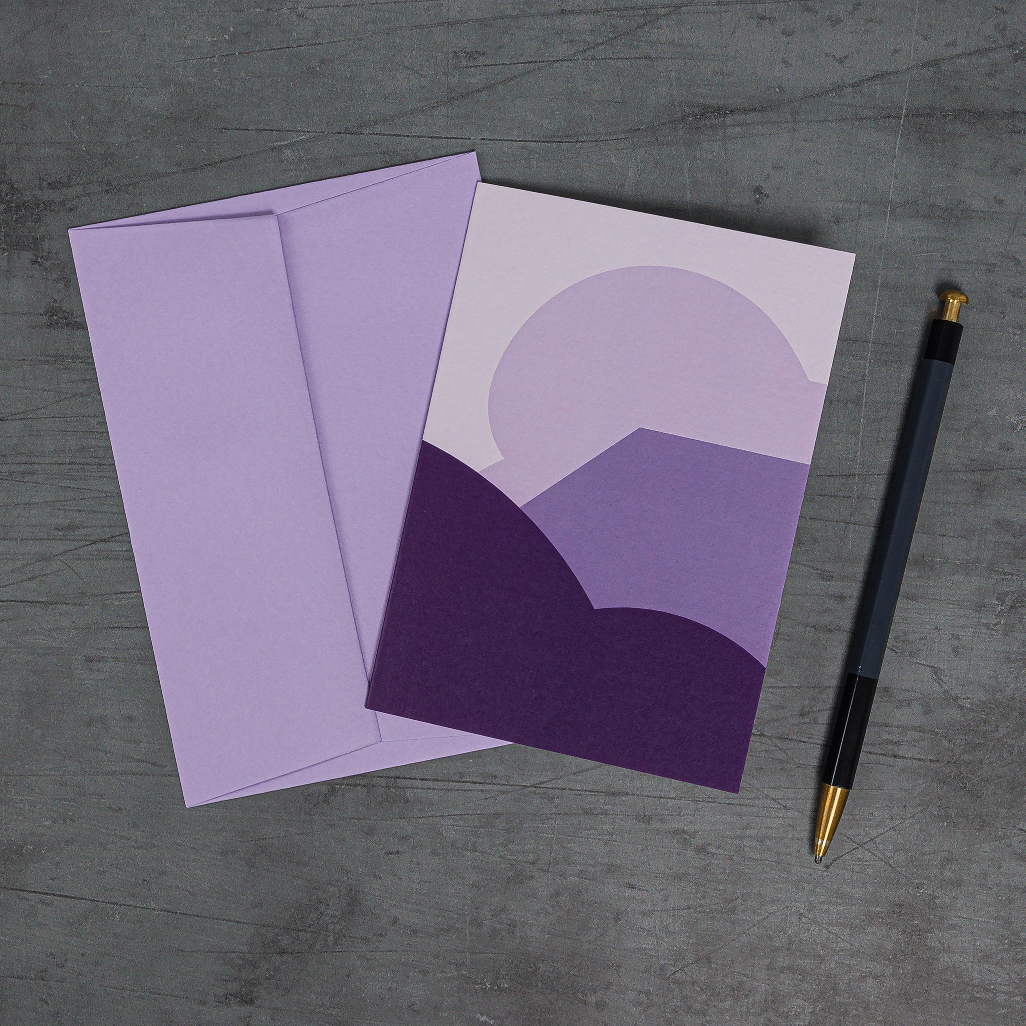 Aerial view, slanted, of Stack (purple) greeting card and matching lilac G F Smith envelope. Design: schematised 'landscape' of stacked curves and angles
