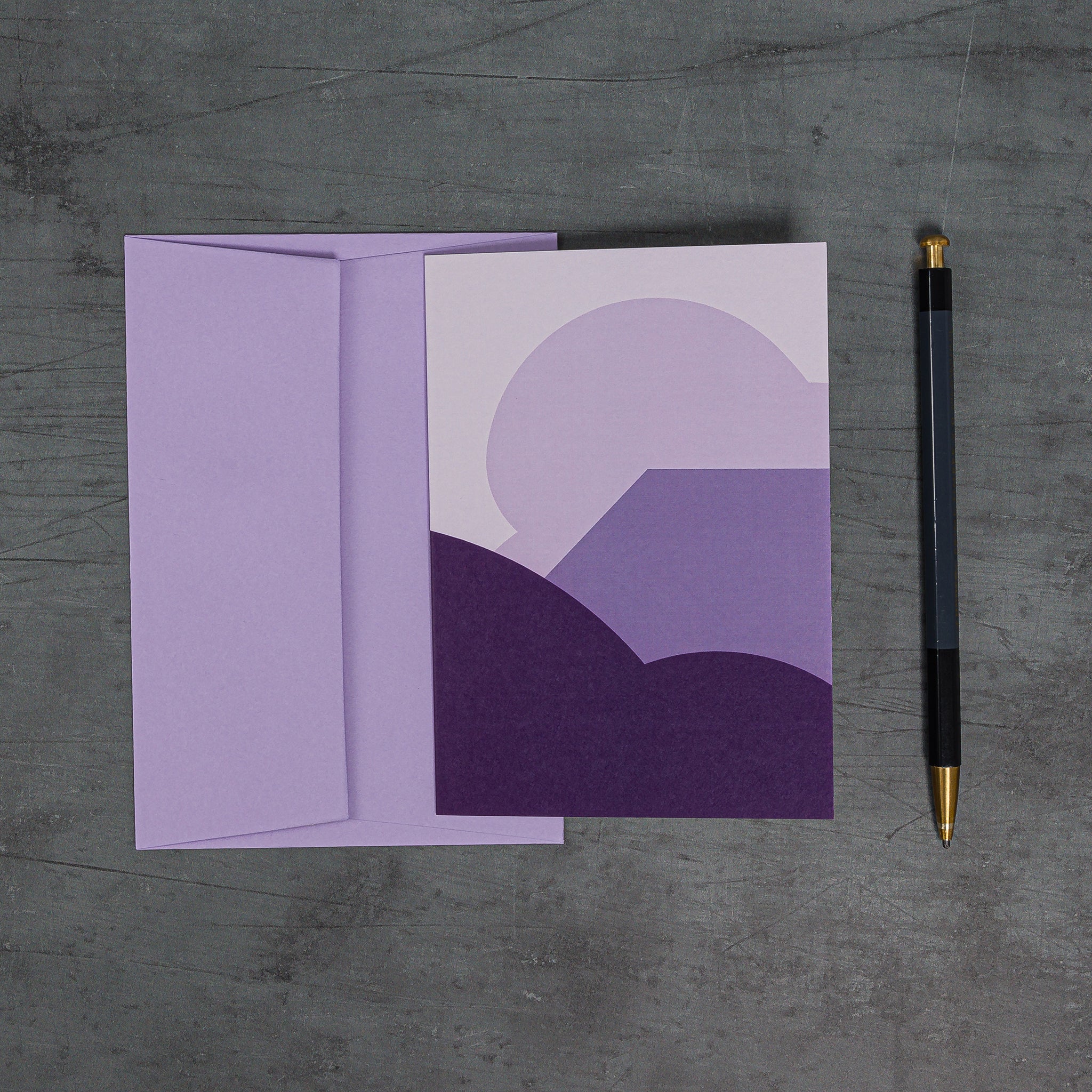 Overhead view of Stack (purple) greeting card and lilac envelope. A stack of sweeping curves and angles resembling a schematic landscape